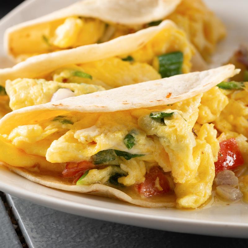 Breakfast tacos filled with scrambled eggs, tomatoes, onions, spinach and cheese